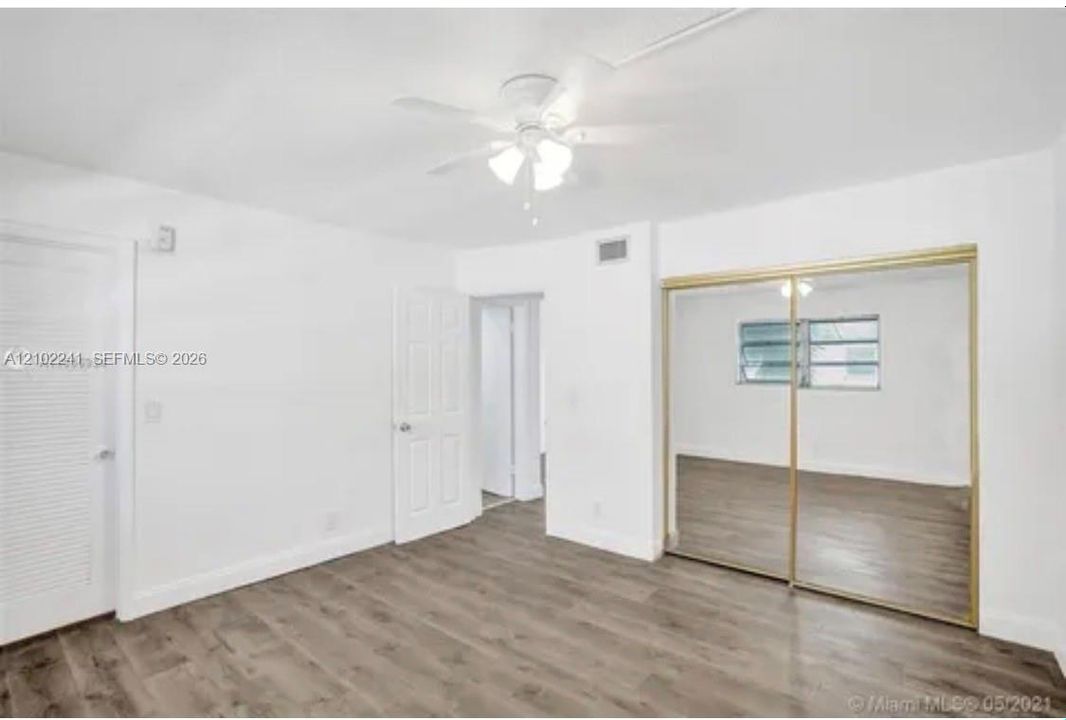 Wood-finish flooring, ceiling fan with integrated lighting, and sliding mirrored closet doors