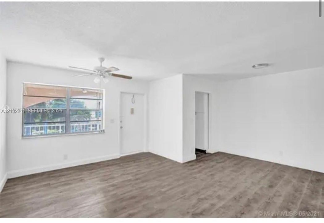Neutral interior featuring wood-finish flooring, a multi-pane horizontal sliding window, a white single-panel entry door, and a ceiling-mounted fan with integrated light fixture