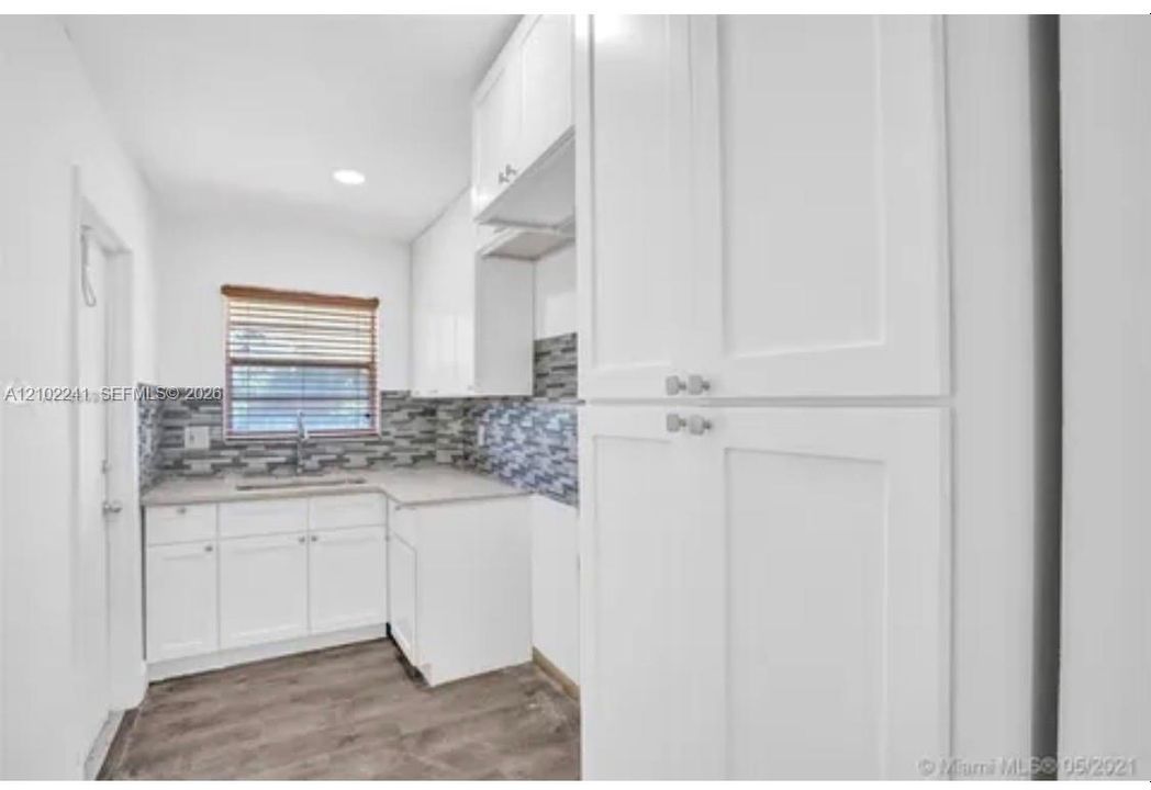 Kitchen featuring white shaker-style cabinetry, a floor-to-ceiling pantry, stone-patterned tile backsplash, neutral countertops, and wood-finish flooring