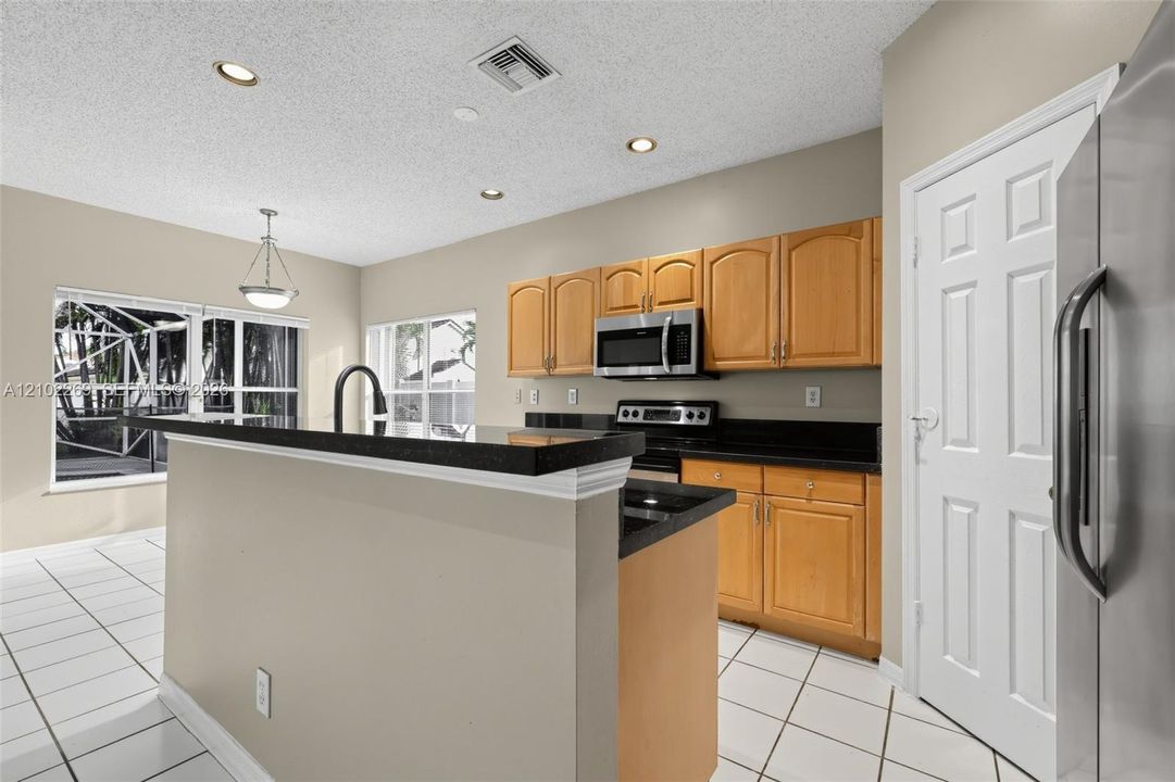 Kitchen featuring wood cabinetry, stone countertops, stainless steel appliance suite, recessed lighting, and tile flooring