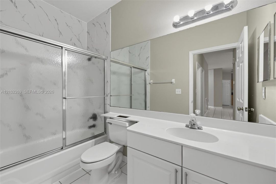 Bathroom featuring a white vanity with a solid surface countertop, an integrated oval sink, a full-width wall mirror, and a tub-shower combination with patterned wall surround and sliding glass doors
