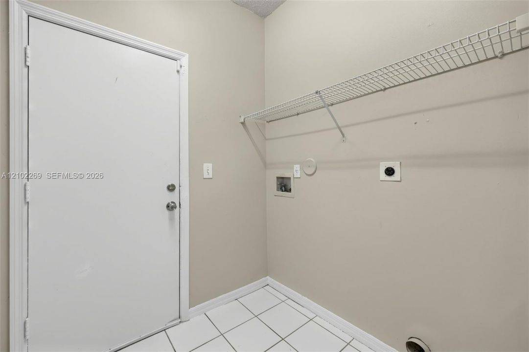 Utility area featuring white ceramic tile flooring, a solid core door, and wall-mounted wire shelving