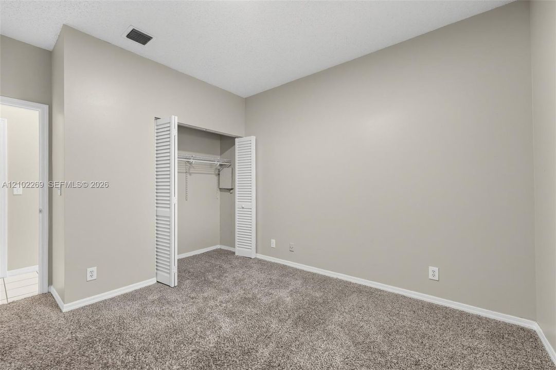 Neutral-toned interior space featuring neutral carpeting, a built-in closet with bi-fold louvered doors, and wire shelving