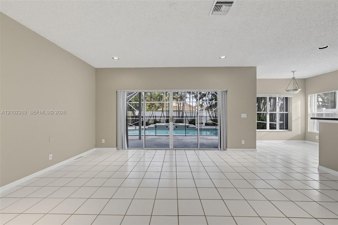 Open-concept space featuring large-format ceramic tile flooring, recessed lighting, and expansive glass sliding doors providing visibility to a screened-in pool and spa area