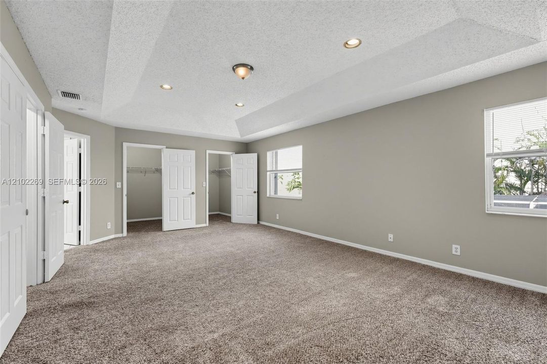 Spacious interior featuring a tray ceiling, recessed lighting, wall-to-wall carpeting, and two built-in closet spaces with six-panel doors
