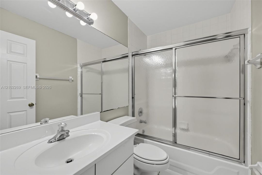 Bathroom featuring a white vanity with an integrated sink, a full-width vanity mirror, a multi-bulb light fixture, and a tub-shower combination with sliding glass doors