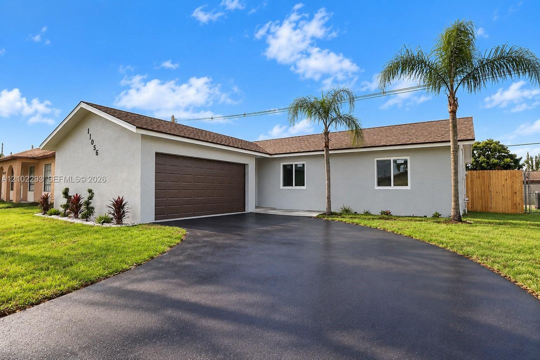 Single-story exterior featuring a stucco facade, an attached two-car garage, asphalt driveway, asphalt shingle roof, and established palm trees