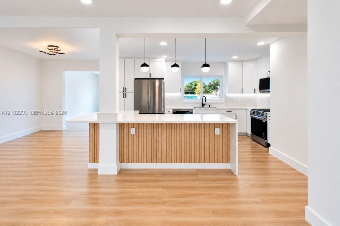 Kitchen featuring a tiered waterfall-edge island with slatted wood detailing, white shaker-style cabinetry, stainless steel appliances, recessed lighting, and wood-finish flooring