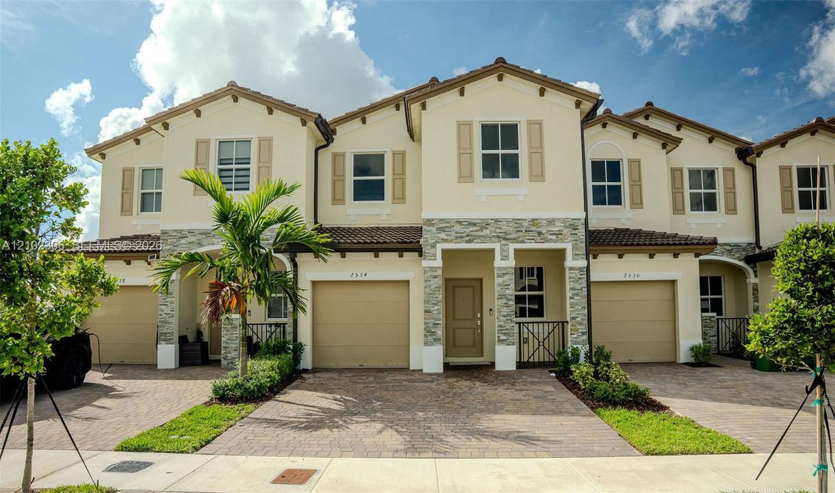 Mediterranean-style exterior featuring stucco finish, stone veneer accents, paver driveway, attached garage, and tiled roof