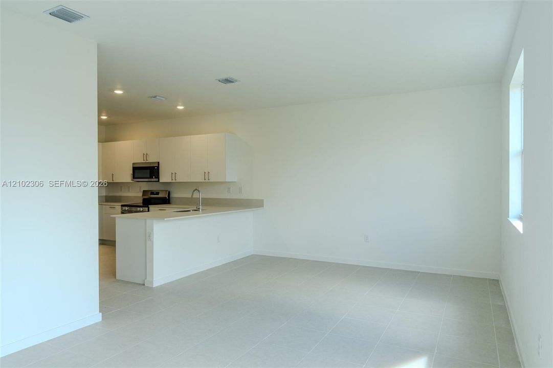 Open-concept area featuring tile flooring, recessed lighting, and kitchen equipped with white cabinetry, stainless steel appliances, and a solid-surface breakfast bar