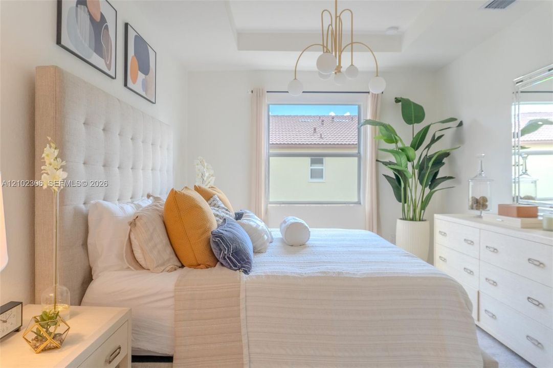 Bedroom featuring a tray ceiling, modern multi-globe chandelier, and large window with neutral-toned drapery