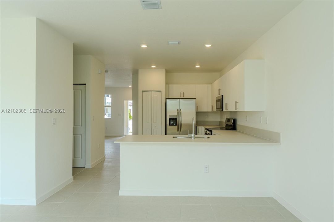 Kitchen featuring white flat-panel cabinetry, a peninsula with a stainless steel sink, tile flooring, recessed lighting, and stainless steel appliances