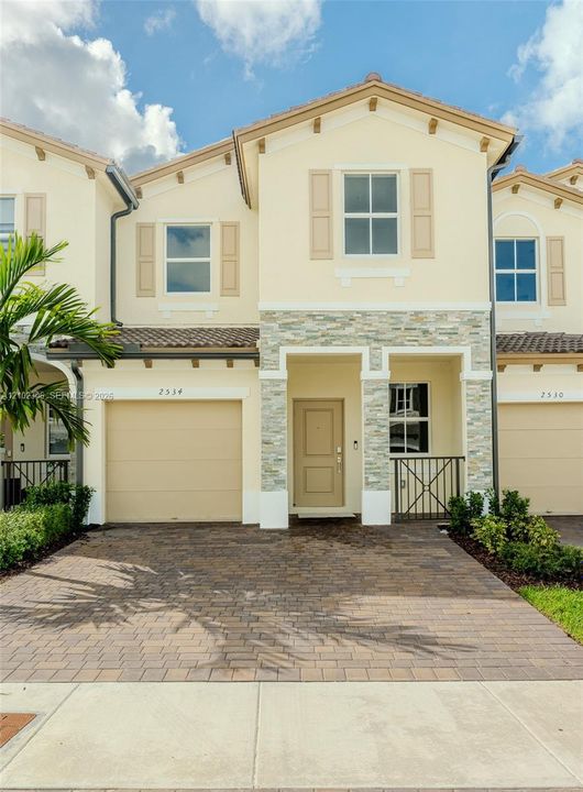 Two-story exterior featuring a stone veneer facade, paver driveway, tiled roof, and decorative shutters