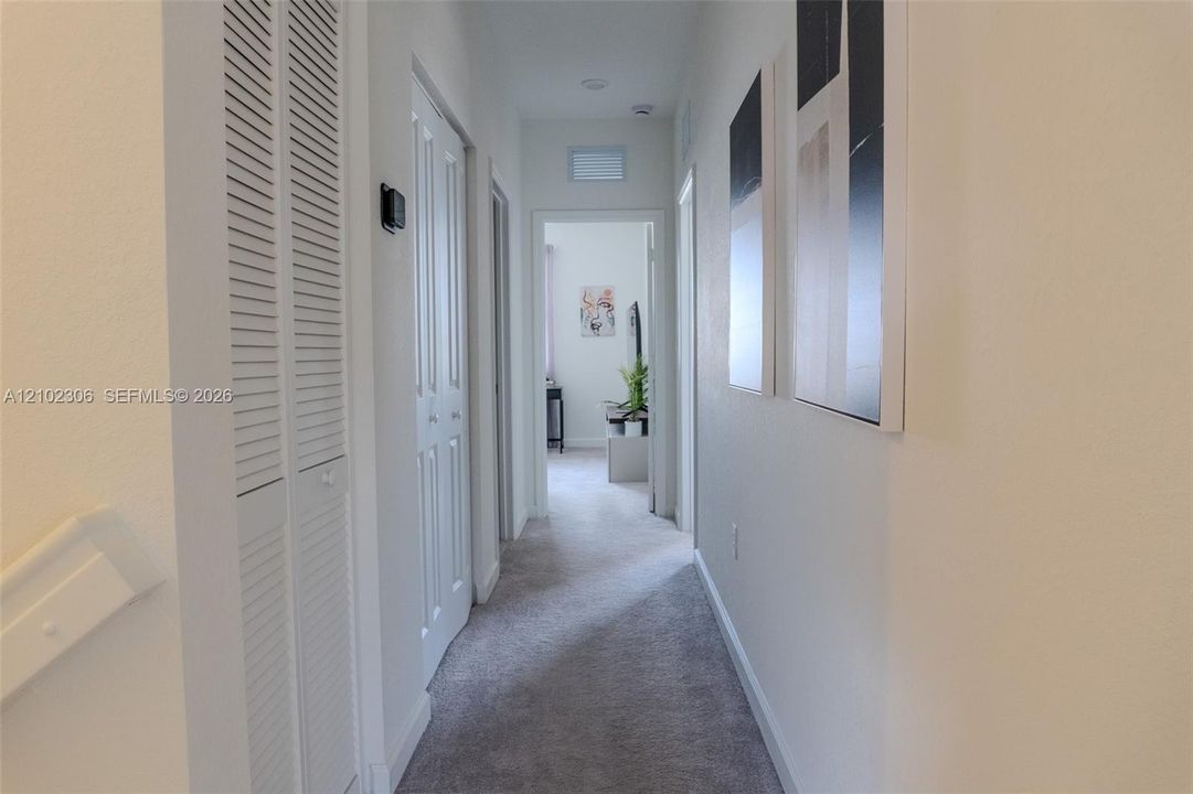Hallway featuring neutral wall-to-wall carpeting, white louvered-style bi-fold closet doors, and recessed ceiling lighting