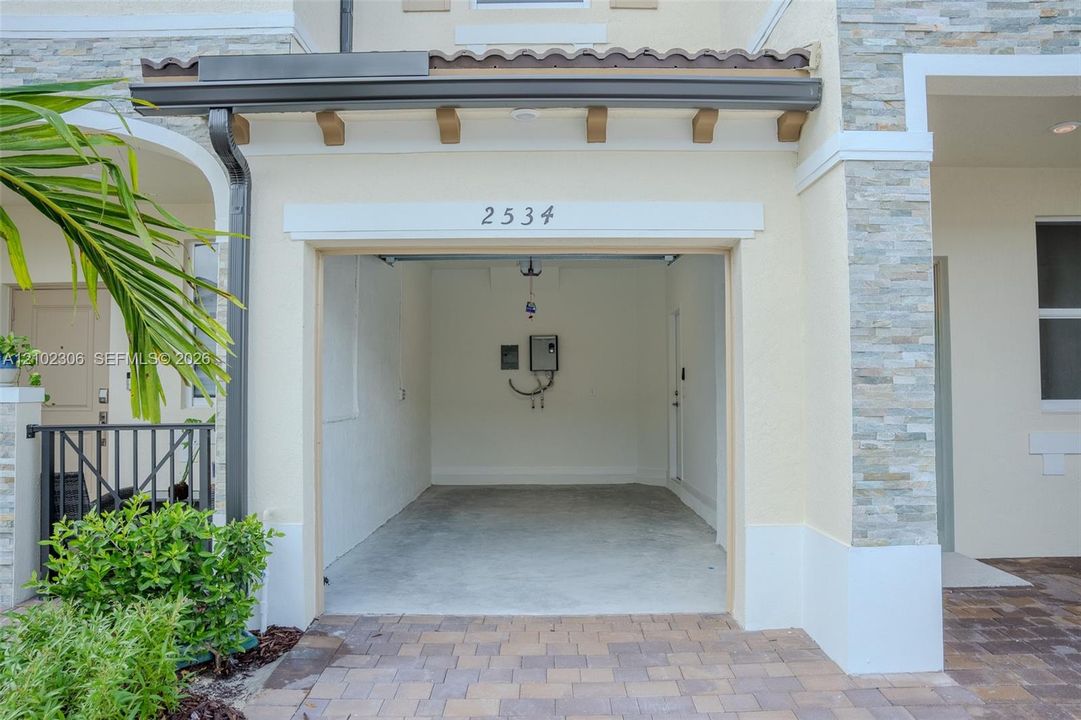 Attached garage featuring stacked stone exterior accents, a concrete floor, and a paver driveway
