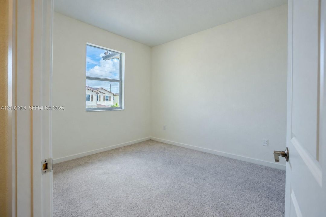 Neutral-toned interior space featuring light-colored wall-to-wall carpeting, a single-pane window, and a paneled interior door with a brushed nickel lever handle