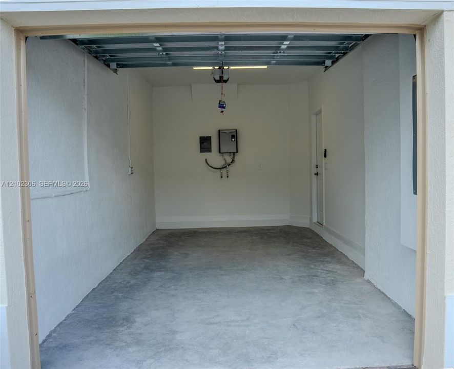 Enclosed garage featuring a concrete floor, finished white walls, a mounted water heater, and a side-entry door