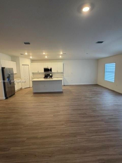 Open-concept kitchen featuring white shaker cabinetry, a center island with a solid surface countertop, wood-finish flooring, and stainless steel appliances