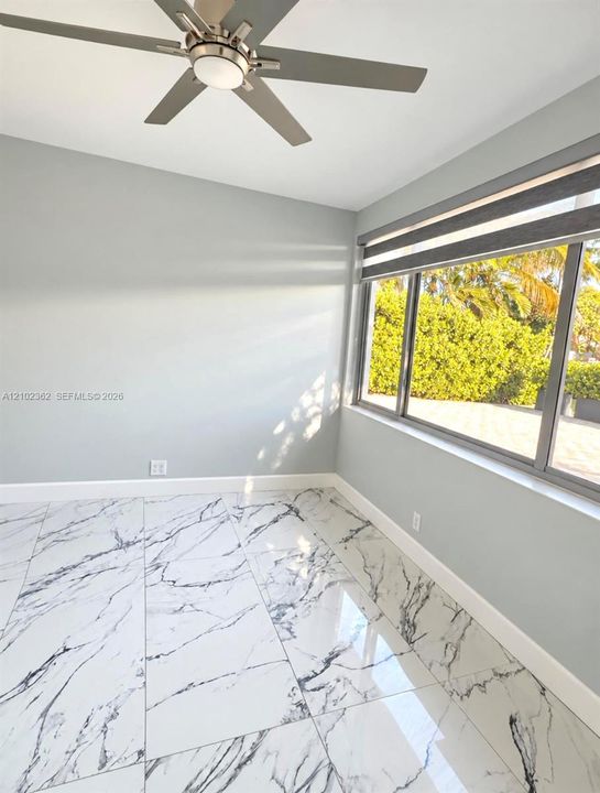 Polished large-format tile flooring with veined detailing, multi-pane window with dark-toned framing, and central ceiling fan with integrated lighting