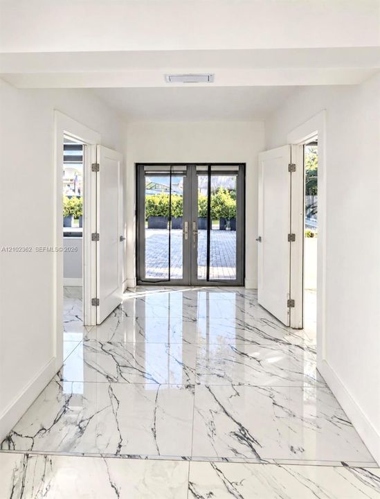 Large-format polished tile flooring with marble-pattern veining, double glass-paneled exterior doors with dark metal framing, and white interior swing doors featuring brushed metal hardware