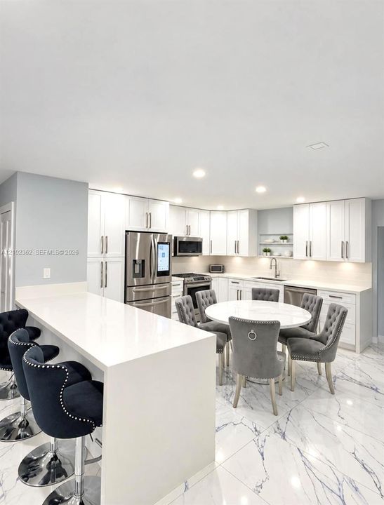 Kitchen featuring white cabinetry, quartz countertops, a waterfall-edge island, stainless steel appliances, and large-format tile flooring with marble-pattern veining