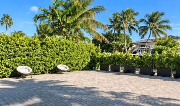 Paver patio featuring integrated perimeter hedging, mature palm trees, and dark-toned modular planters