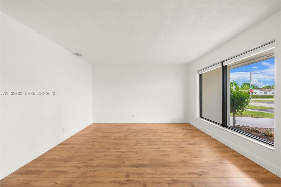Neutral-toned interior space featuring wood-finish flooring, a expansive picture window with black frames, and recessed lighting