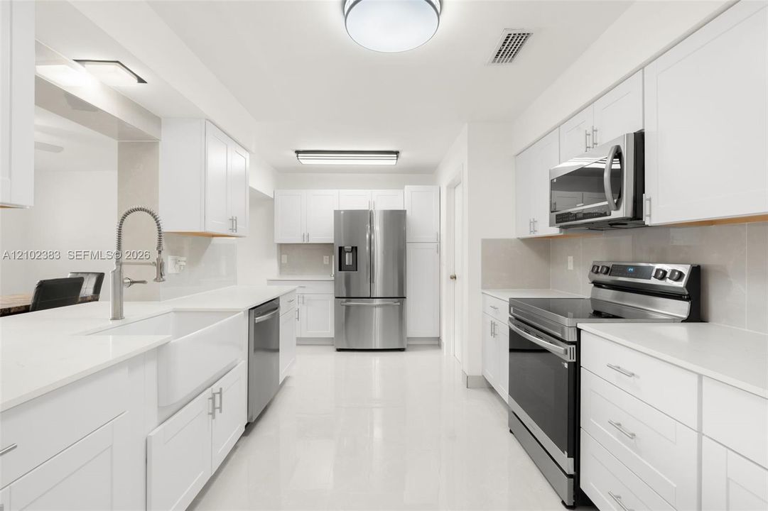 Kitchen featuring white cabinetry, solid-surface countertops, farmhouse sink with arched faucet, stainless steel appliances, and tile flooring