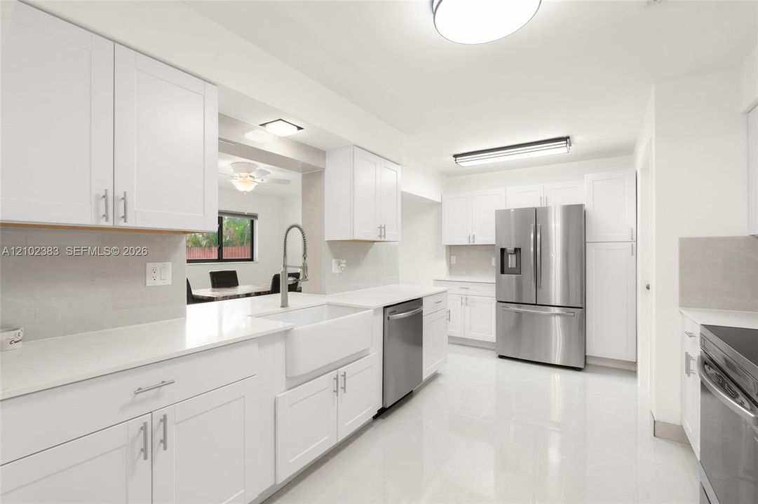 Kitchen featuring white cabinetry, quartz countertops, a farmhouse-style apron sink, stainless steel appliances, and tile flooring