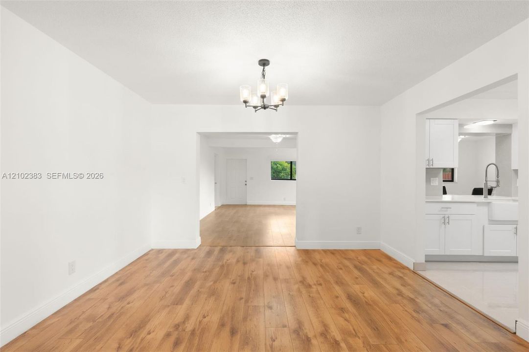 Dining area featuring wood-finish flooring, a contemporary multi-light chandelier, and white cabinetry with a farmhouse-style sink