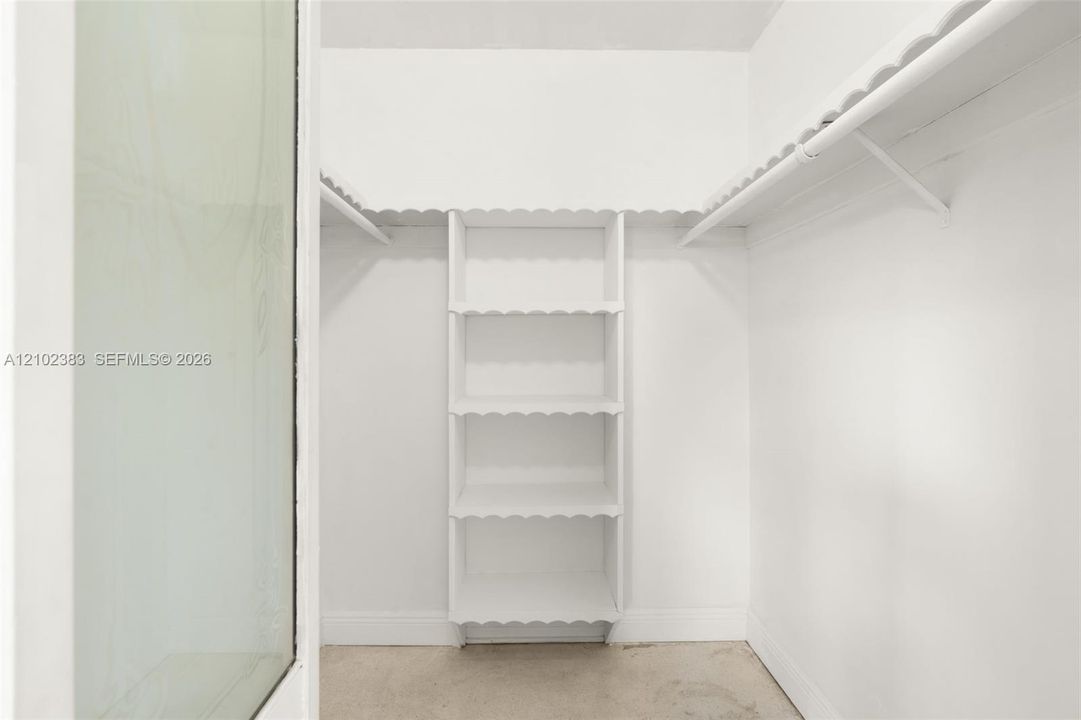 Primary walk-in closet featuring white built-in shelving, scalloped-edge wood trim, and a hanging rod