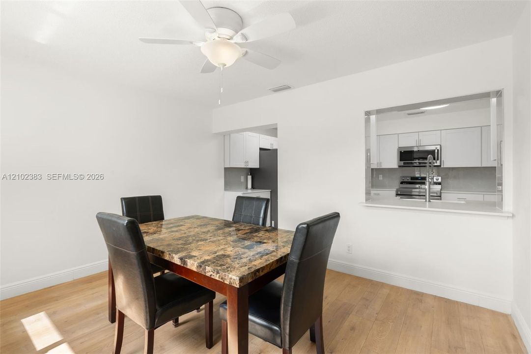 Breakfast area featuring wood-finish flooring, a ceiling fan with integrated lighting, and a kitchen passthrough with a countertop ledge