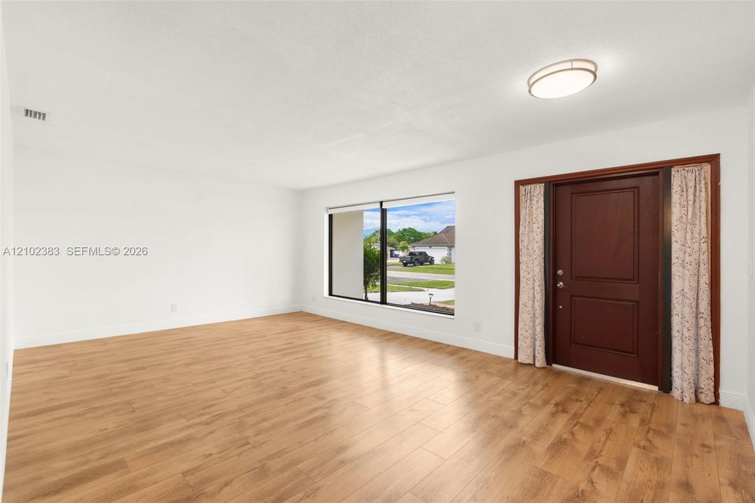 Interior space featuring wood-finish flooring, a large picture window, a solid wood-panel entry door, and a flush-mount ceiling light fixture