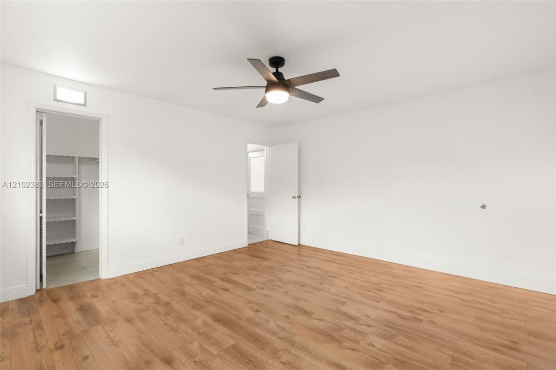 Primary bedroom Wood-finish flooring, multi-blade ceiling fan with integrated light, and walk-in closet with built-in shelving