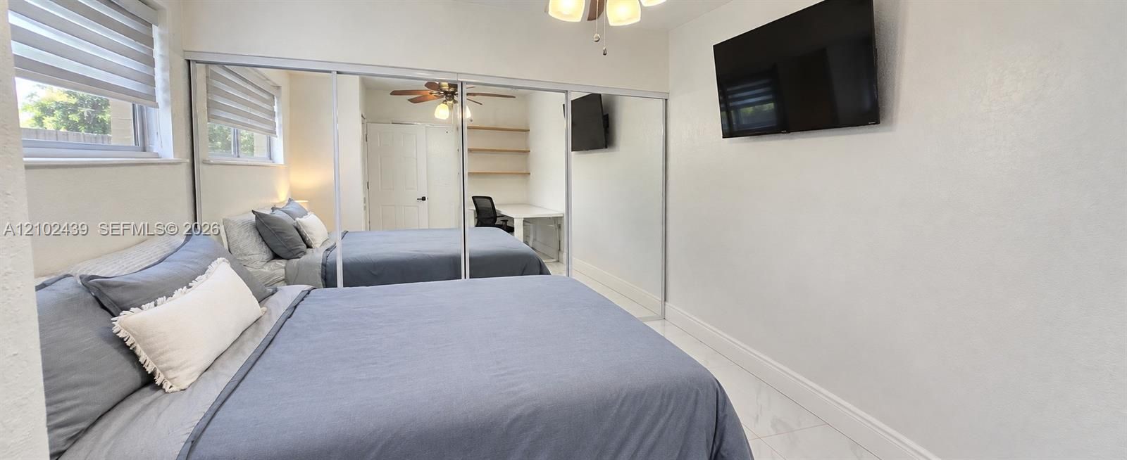 Recessed windows with horizontal blinds, full-length mirrored closet doors, and a ceiling fan with integrated lighting