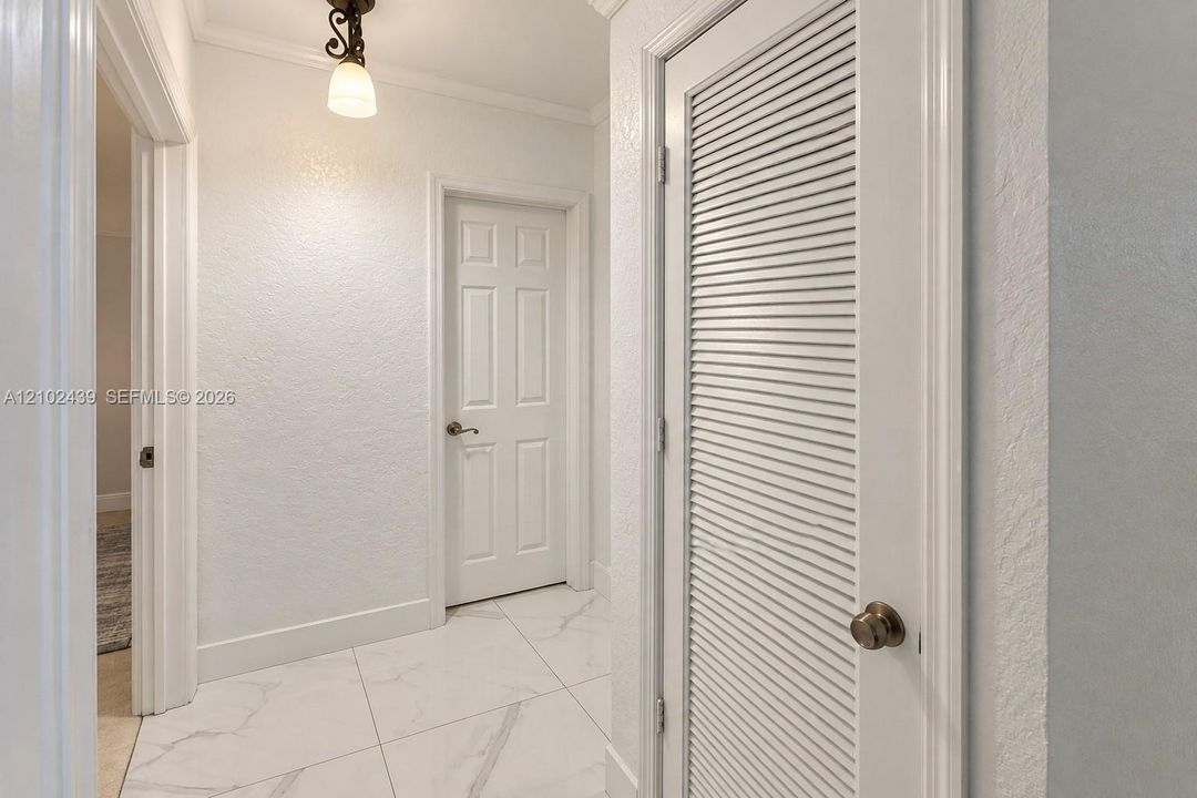 White tile flooring, crown molding, a built-in louvered door, a six-panel door, and a decorative ceiling light fixture