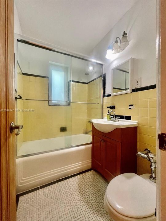 Bathroom featuring a vanity with an integrated basin, a soaking tub with sliding glass doors, tiled walls with decorative trim, and geometric patterned floor tile
