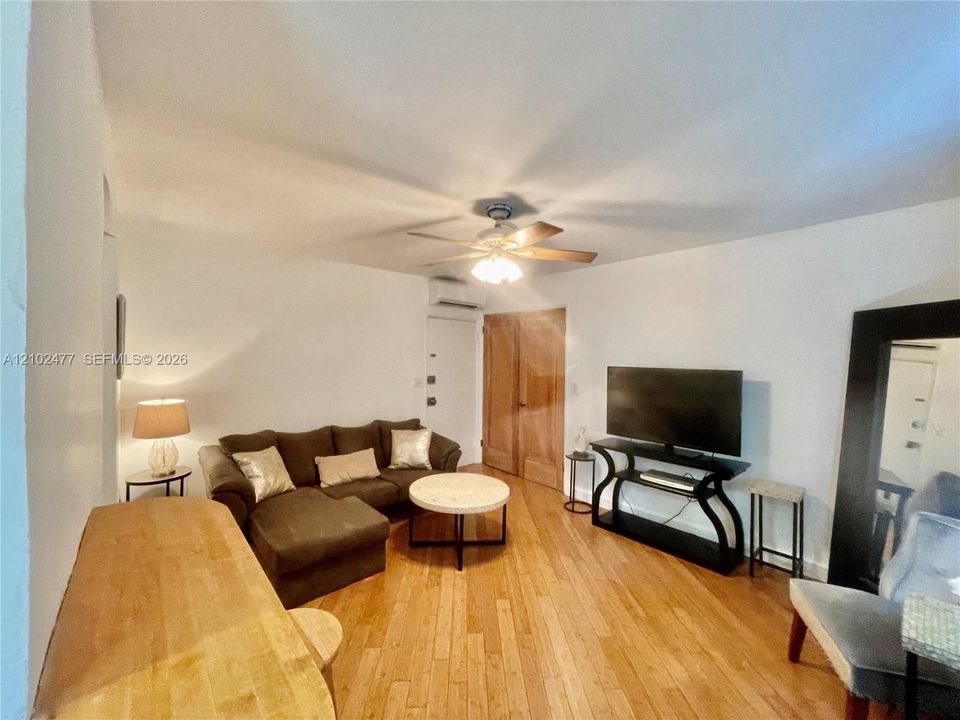 Wood-finish flooring, ceiling fan with integrated light fixture, wall-mounted climate control unit, and wood-paneled interior doors