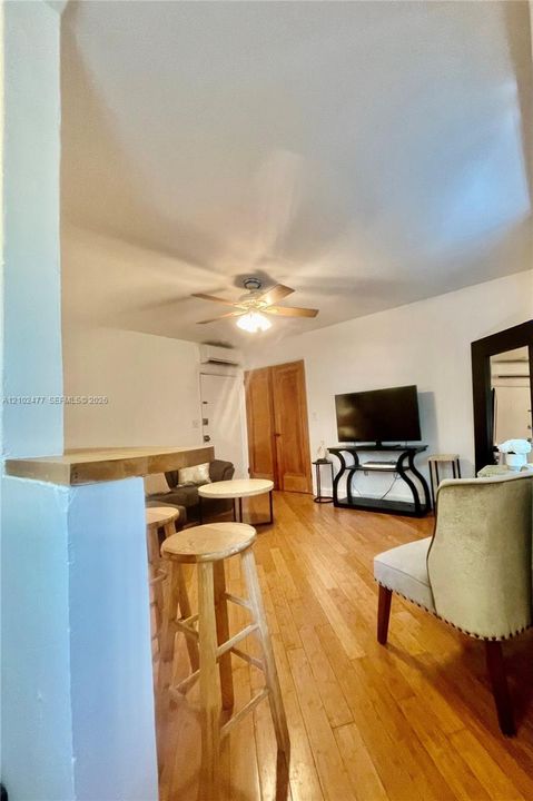 Living area featuring wood-finish flooring, a ceiling fan with integrated light fixture, a wood-surfaced breakfast bar, and wood-paneled interior doors