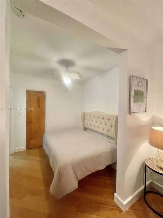 Interior space featuring wood-finish flooring, a ceiling-mounted fan with light fixture, and a solid wood-panel door