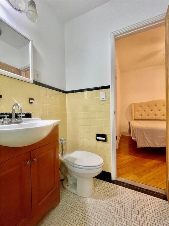 Bathroom featuring a pedestal-style vanity with an integrated basin, chrome faucet, wall-mounted mirror, and decorative tile wainscoting with a black tile accent border