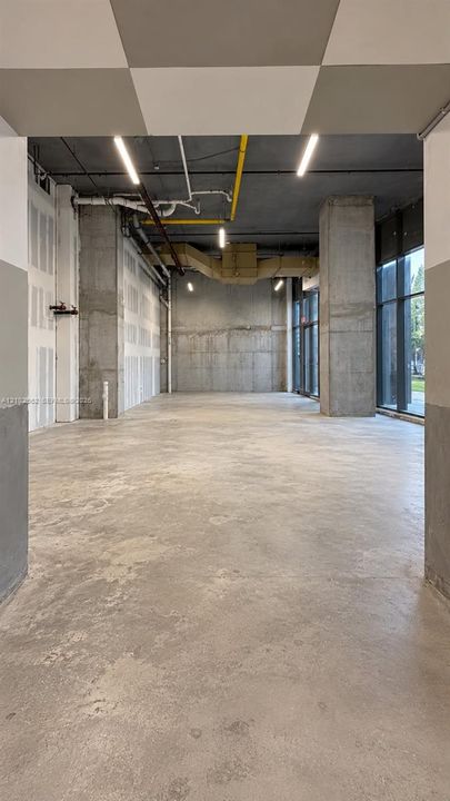 Open-concept interior featuring concrete flooring, exposed industrial ceiling, floor-to-ceiling glass paneling, and structural concrete columns