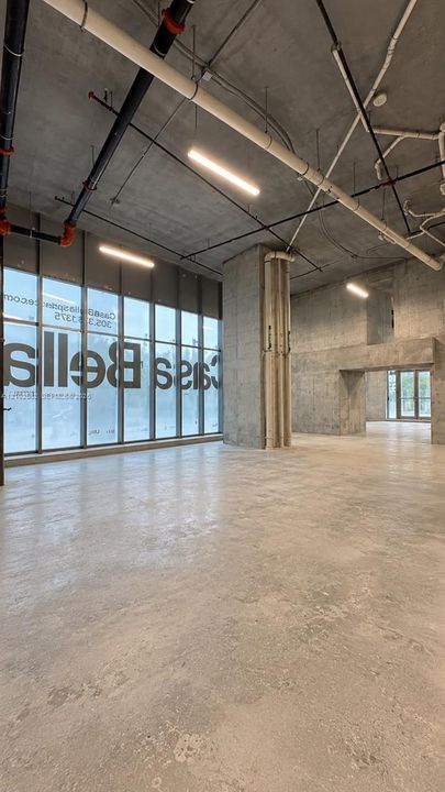 Industrial-style interior featuring exposed concrete ceilings, polished concrete flooring, floor-to-ceiling glass paneling, and suspended linear lighting fixtures
