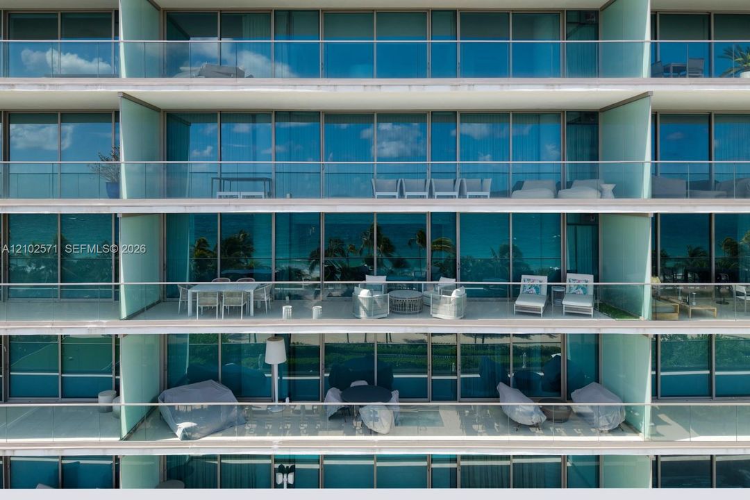 Multi-level residential exterior featuring floor-to-ceiling glass paneling, horizontal cantilevered balconies, and glass-railing balustrades