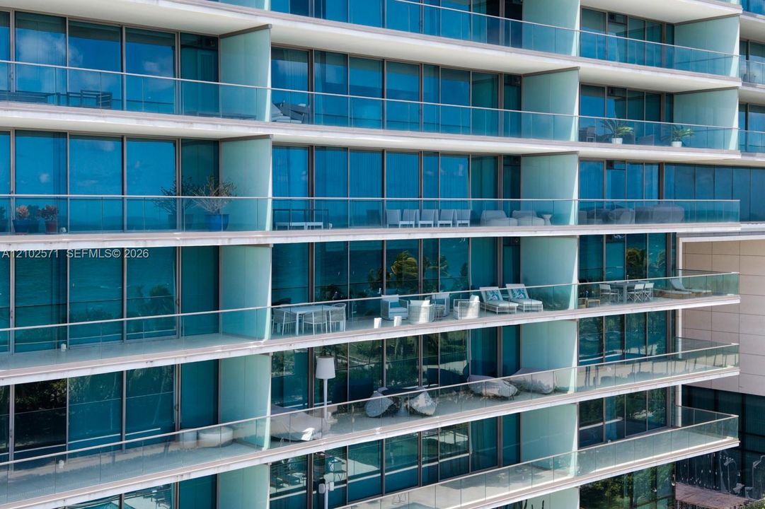 High-rise facade featuring floor-to-ceiling blue-tinted windows, full-width glass-railed balconies, and concrete slab terrace dividers
