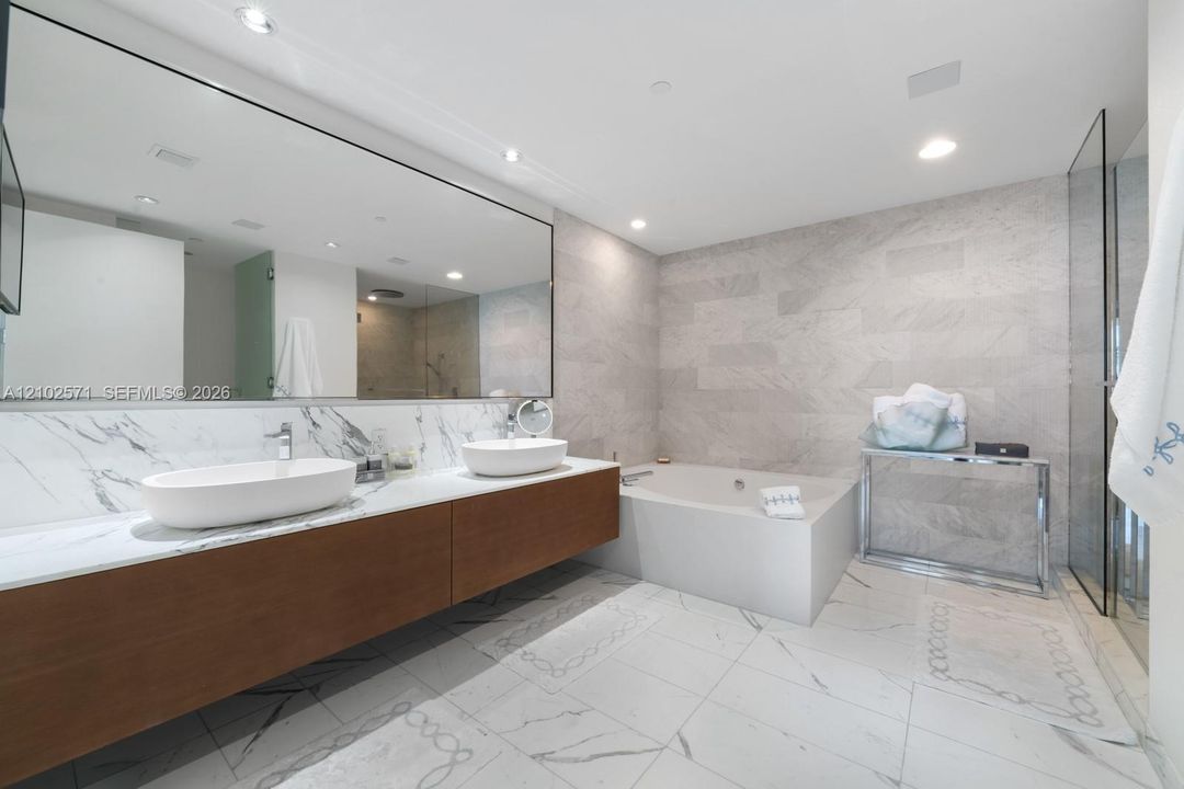 Floating wood-finish vanity with dual vessel sinks, expansive wall-mounted mirror, soaking tub, and tile flooring