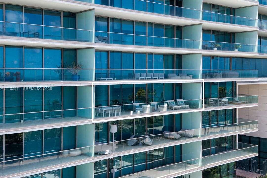 High-rise exterior featuring floor-to-ceiling blue-tinted glass windows and expansive private balconies with frameless glass railings