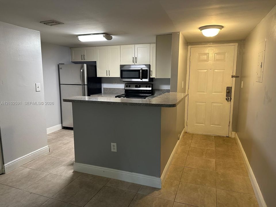 Kitchen featuring white cabinetry, stone-finish countertops, stainless steel appliances, a breakfast bar, and tile flooring