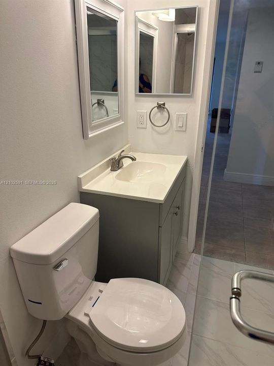 Bathroom featuring a gray vanity with an integrated basin, chrome faucet, rectangular wall-mounted mirror, and tile flooring