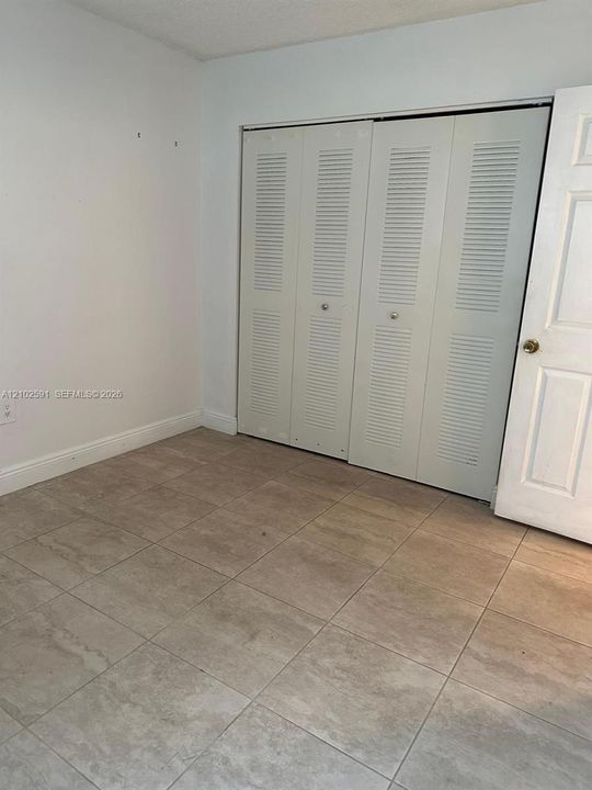 Neutral-toned tile flooring, four-panel louvered closet doors, and six-panel interior swing door
